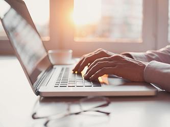 person's hands typing on a laptop at table